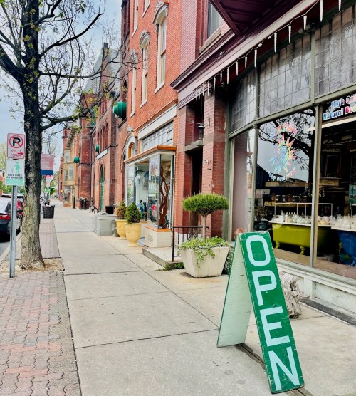 A street view featuring brick buildings, planters, and an "OPEN" sign outside a shop.