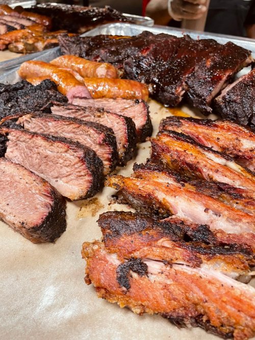 A variety of smoked meats, including brisket, ribs, and sausage, arranged on a tray with a smoky glaze.
