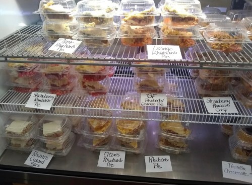 A display case filled with various rhubarb desserts, including pies and bars, each labeled with their names.