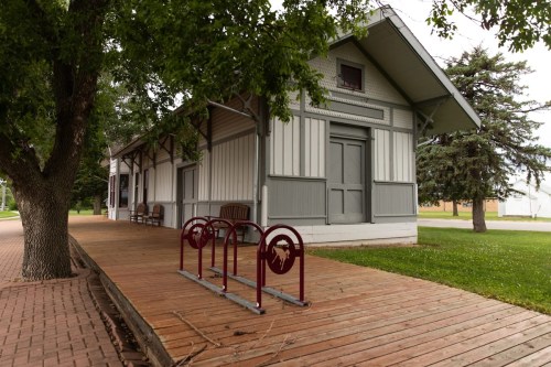 A historic building with a wooden deck and bike rack, surrounded by trees and grass.