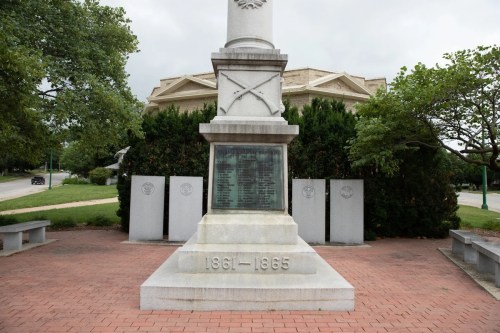 A monument with inscriptions honoring those from 1861-1865, surrounded by greenery and benches.