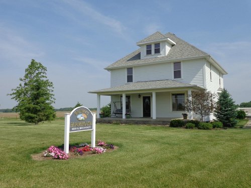 A charming white two-story house with a front porch, surrounded by green grass and colorful flower beds.