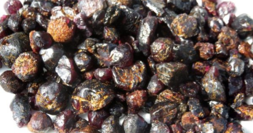 A close-up of a pile of dark, shiny gemstones with hints of red and purple, showcasing their natural textures and shapes.
