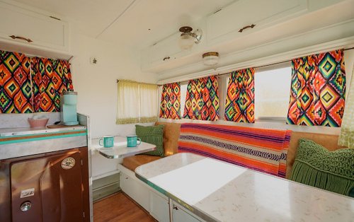 Brightly decorated vintage camper interior with colorful curtains, a cozy seating area, and a small dining table.