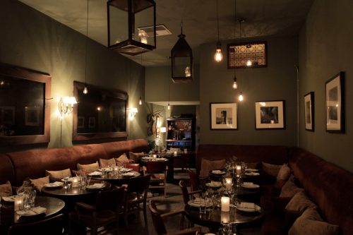 Cozy restaurant interior with dim lighting, wooden tables, and plush seating, creating an inviting atmosphere.
