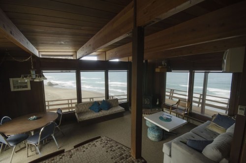 Cozy beach house interior with large windows overlooking the ocean, featuring a dining table and comfortable seating.