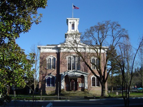 Historic brick building with a clock tower, labeled "Jacksonville Museum," surrounded by trees and a clear blue sky.