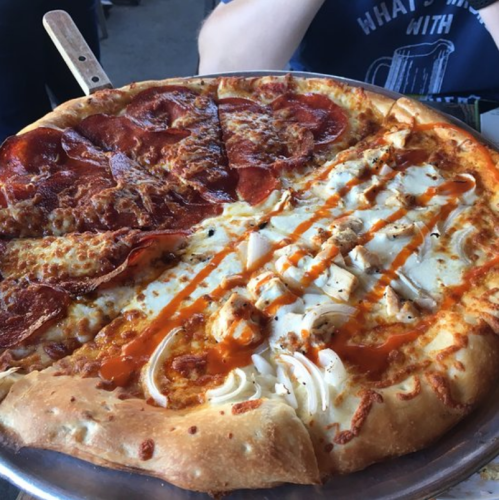 A large pizza divided into two halves: one with pepperoni and cheese, the other with white sauce and drizzled toppings.