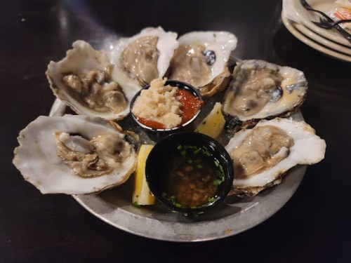 A plate of fresh oysters on the half shell, served with sauces and garnishes.