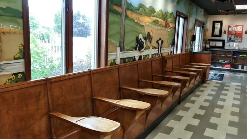 A wooden bench with several empty seats against a mural of a countryside scene and large windows.