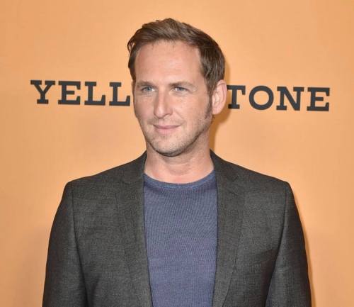 A man in a dark blazer and blue shirt poses against a yellow background with the word "YELLOWSTONE" prominently displayed.