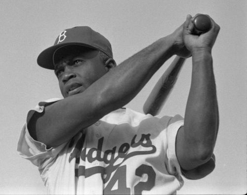 A Black baseball player in a Dodgers uniform, holding a bat and preparing to swing, against a clear sky.