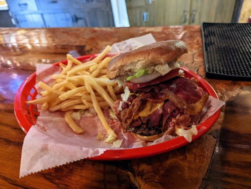 A hearty burger stacked with bacon and cheese, served with a side of golden fries on a red plate.