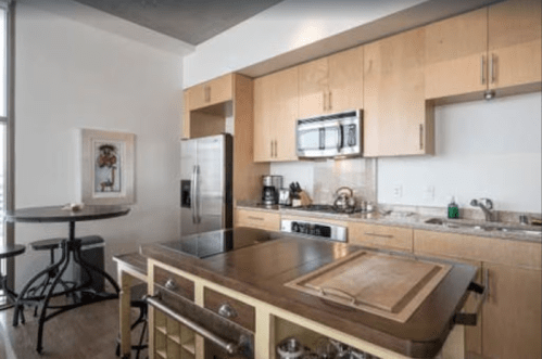 Modern kitchen with wooden cabinets, stainless steel appliances, and a small dining table by the window.