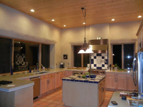 Spacious kitchen with wooden ceiling, tile accents, and modern appliances, featuring a large island and ample natural light.