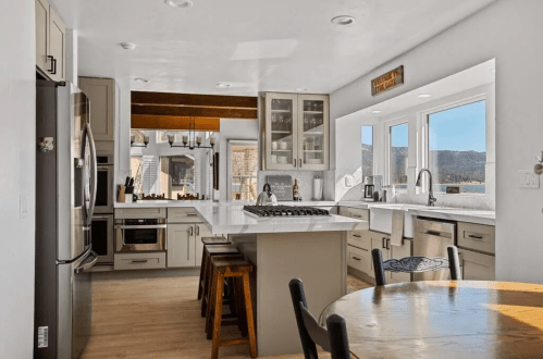 Modern kitchen with white cabinets, a large island, stainless steel appliances, and a dining table by the window.