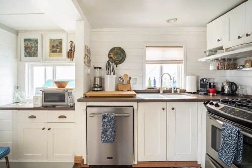 Cozy kitchen with white cabinets, stainless steel appliances, and a window above the sink, featuring decorative wall art.