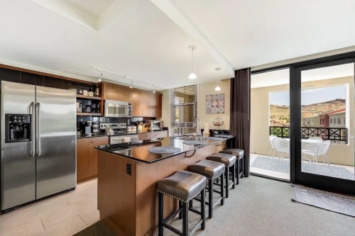 Modern kitchen with stainless steel appliances, dark wood cabinets, and a bar with stools, overlooking a balcony.
