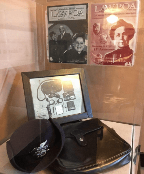 Display case featuring historical police memorabilia, including a cap, badge, and anniversary publications.