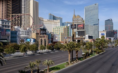 A view of the Las Vegas Strip featuring themed hotels, palm trees, and a clear blue sky.
