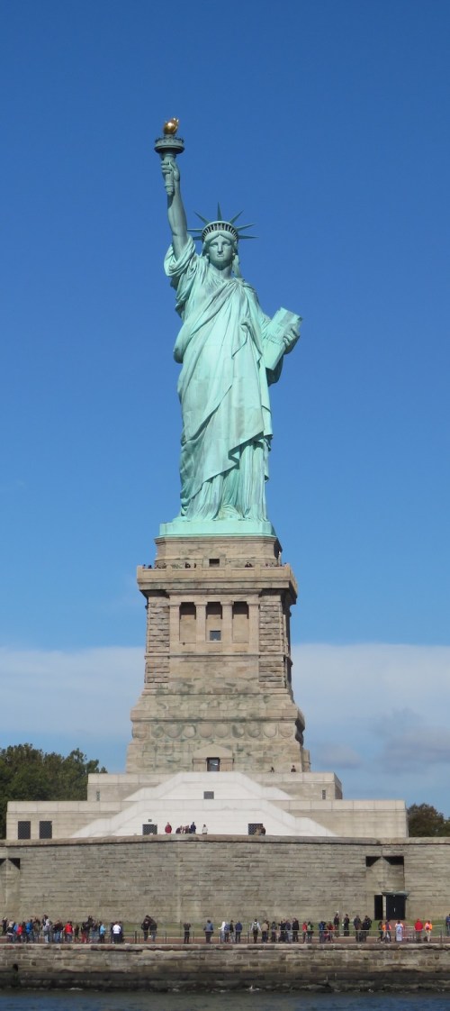 The Statue of Liberty stands tall against a clear blue sky, holding a torch and facing the water.