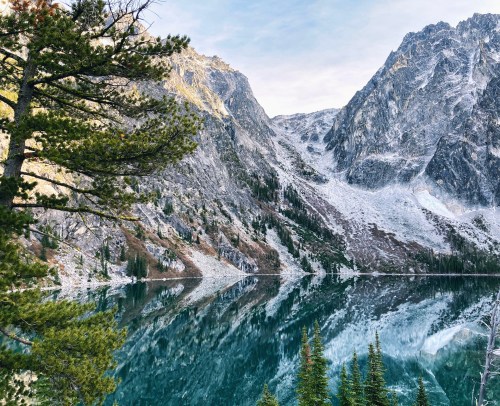 A serene mountain landscape with a reflective lake, surrounded by rocky peaks and evergreen trees.