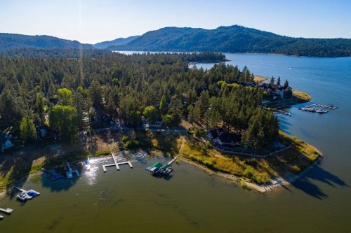 Aerial view of a serene lake surrounded by forested hills and docks, with clear blue water and sunny skies.
