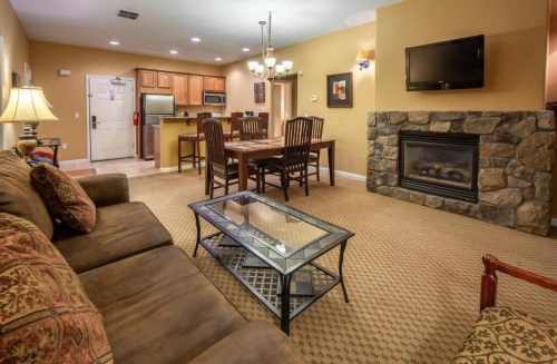 Cozy living area with a sofa, dining table, fireplace, and kitchen in a warm-toned room.