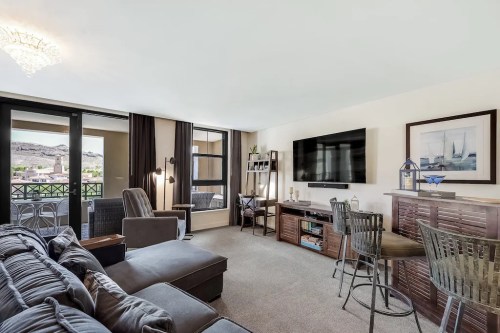 Cozy living room with a sofa, TV, and bar area, featuring large windows and a view of the outdoors.