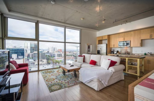 Modern apartment living room with large windows, city views, a cozy sofa, and a stylish kitchen area.