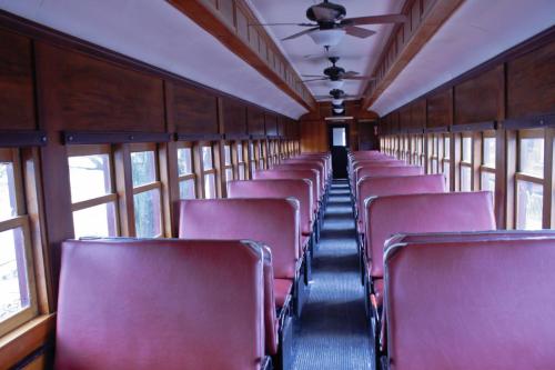Interior of a vintage train car featuring rows of red upholstered seats and large windows.
