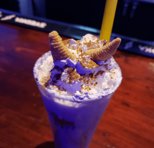 A creamy dessert drink topped with whipped cream, crushed cookies, and two cone-shaped decorations.