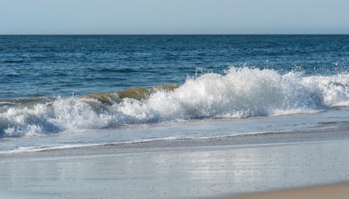 Waves gently crashing on a sandy beach under a clear blue sky.