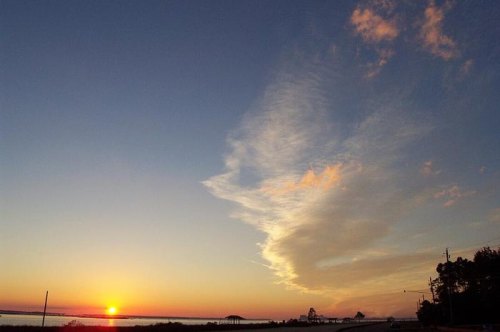 Sunset over a calm body of water, with vibrant colors in the sky and wispy clouds.