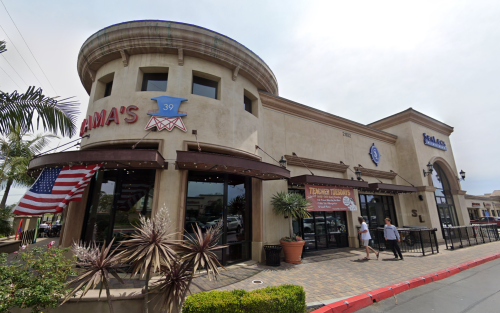 Exterior view of a restaurant with an American flag, featuring a round tower and outdoor seating area.