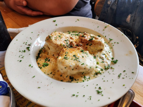 A bowl of creamy biscuits smothered in gravy, garnished with parsley and a sprinkle of paprika.