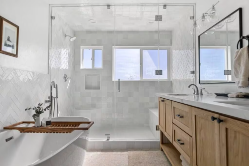 Modern bathroom featuring a glass shower, freestanding tub, wooden vanity, and natural light from large windows.