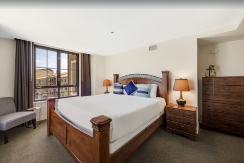 A cozy bedroom featuring a wooden bed, bedside lamps, a dresser, and a large window with a view.