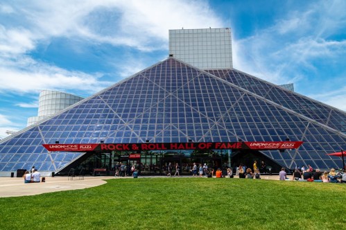 Exterior view of the Rock & Roll Hall of Fame, featuring a glass pyramid structure and green lawn.