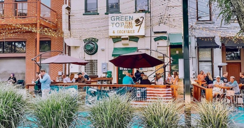 Outdoor dining scene at a restaurant with string lights, people enjoying meals, and an American flag displayed.