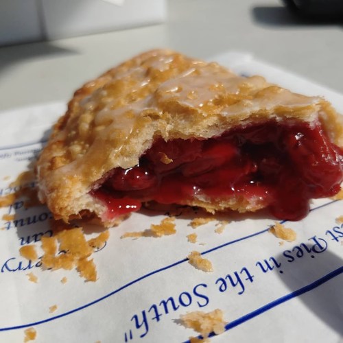 A flaky pastry with a golden crust, filled with bright red cherry filling, resting on a white paper napkin.