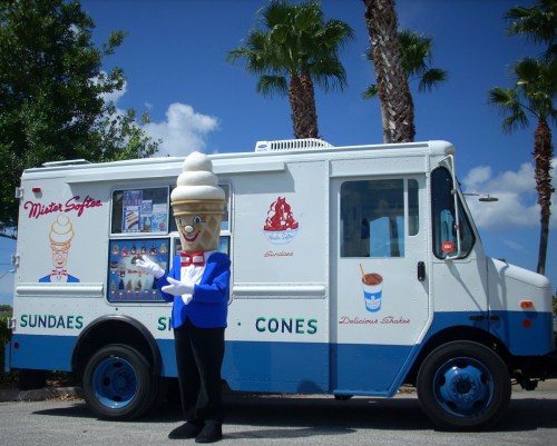 A cheerful ice cream truck with a mascot holding an ice cream cone, surrounded by palm trees under a blue sky.