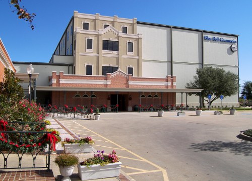 A large building with a decorative entrance, surrounded by flower planters and clear blue skies.