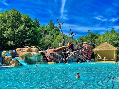 A pirate ship playground partially submerged in a blue pool, surrounded by trees and a clear blue sky.