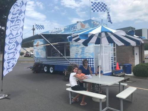 A food truck selling fried pies, with a family sitting at a picnic table under a striped umbrella.