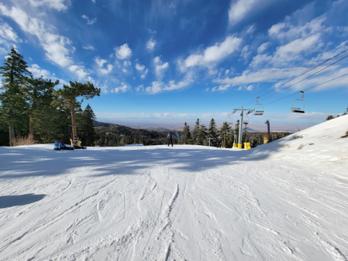 A snowy ski slope with trees, ski lifts, and a clear blue sky in the background.