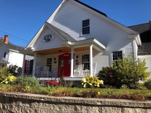 A charming white house with a red door, rocking chairs on the porch, and colorful flowers in the garden.