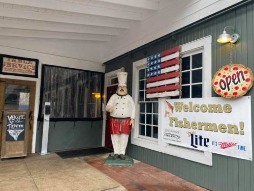 A restaurant entrance featuring a chef statue, an "Open" sign, and a welcome banner for fishermen.