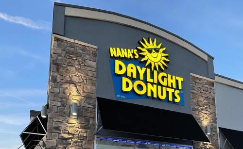Sign for Nana's Daylight Donuts featuring a smiling sun logo, set against a blue sky.