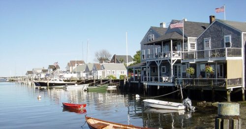 A peaceful waterfront scene with boats and charming houses, featuring American flags and calm water reflections.